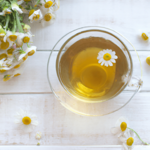 Healthy chamomile tea in a glass teacup on white wooden background