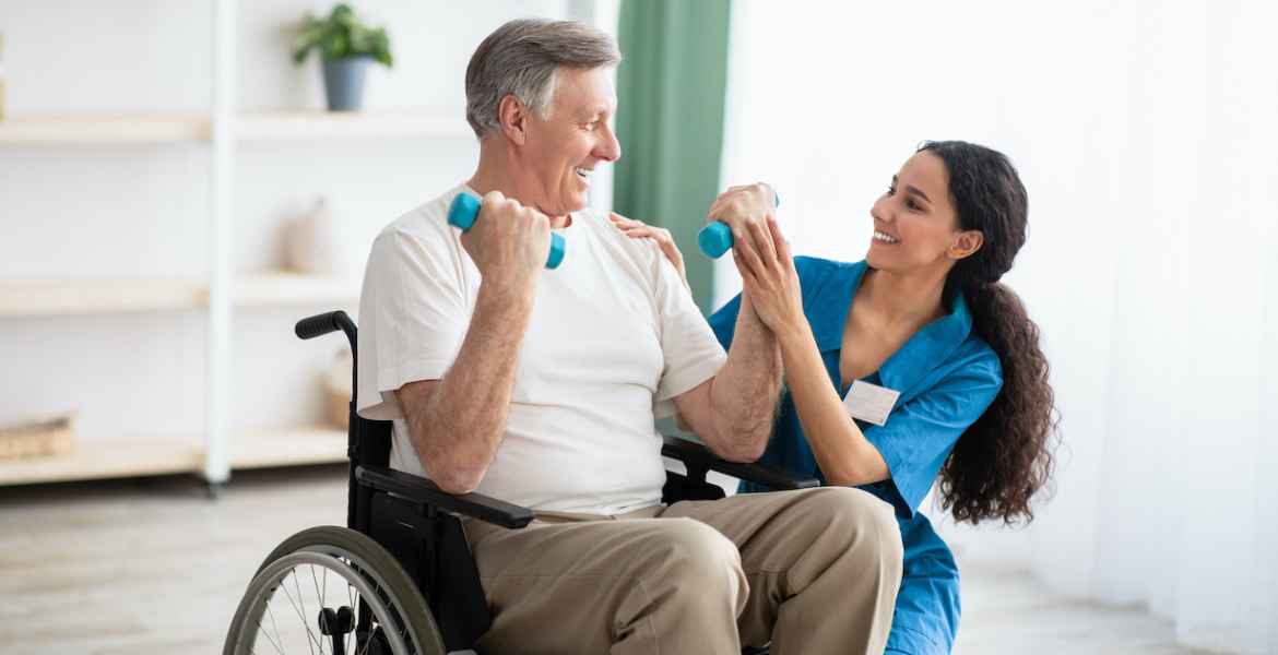 doctor helping disabled elderly man in wheelchair to work out with dumbbells, to recover from injury at health centre