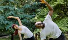 active healthy couple, african guy and caucasian girl, working out together outdoors, doing stretching exercises on the grass. sport and fitness concept. focus on woman behind