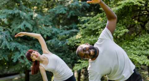 active healthy couple, african guy and caucasian girl, working out together outdoors, doing stretching exercises on the grass. sport and fitness concept. focus on woman behind