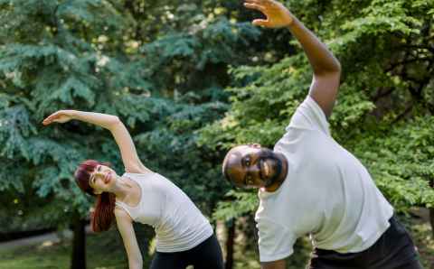 active healthy couple, african guy and caucasian girl, working out together outdoors, doing stretching exercises on the grass. sport and fitness concept. focus on woman behind