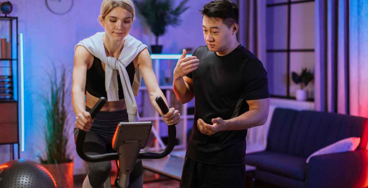 young female wearing sport bra and using exercise bike and her trainer asian male.