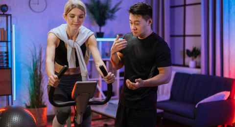 young female wearing sport bra and using exercise bike and her trainer asian male.