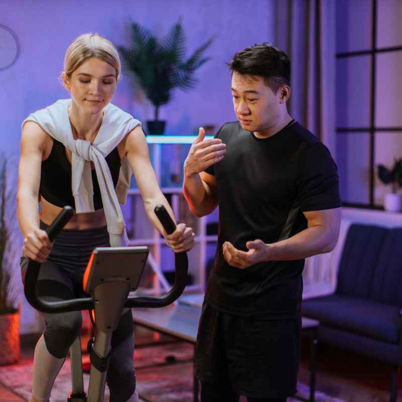 young female wearing sport bra and using exercise bike and her trainer asian male.